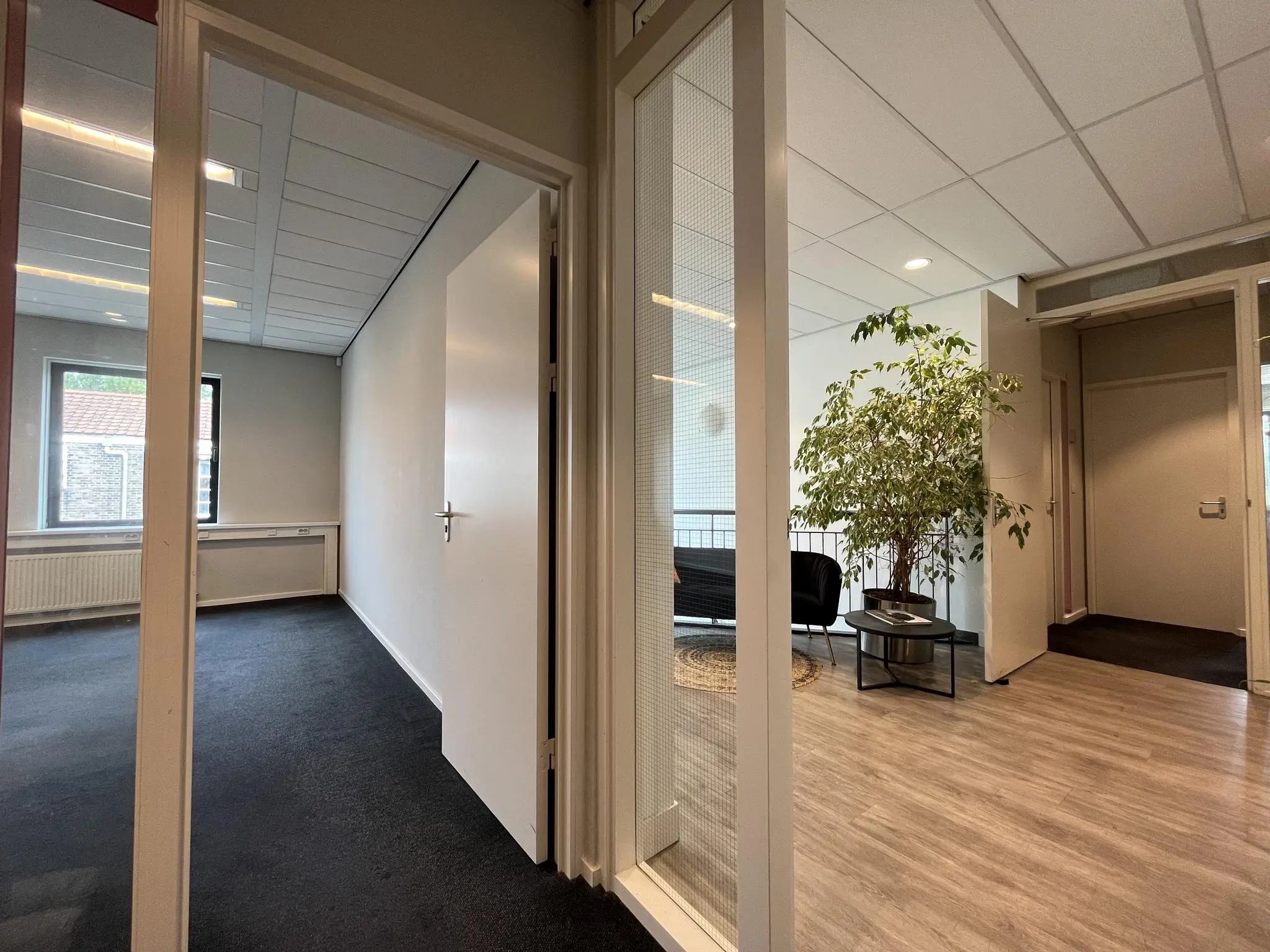 Binnenzicht van een kantoorpand aan de Kanaalweg met een lege kamer links en een wachtruimte met planten en stoelen rechts.