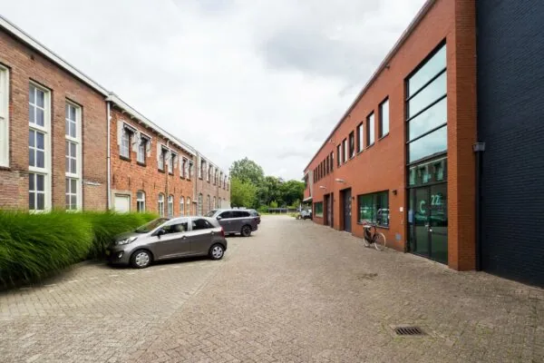 Binnenplein aan de Kanaalweg met geparkeerde auto's tussen een oud en een modern bakstenen gebouw.