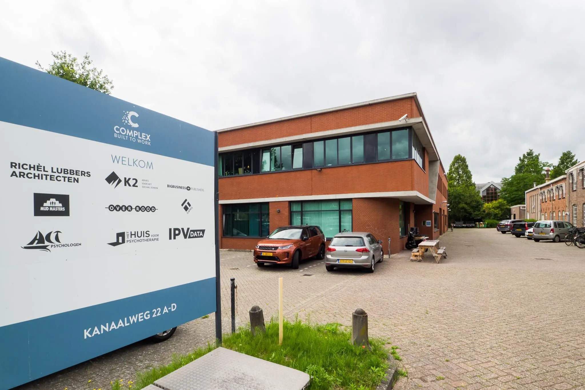 Bedrijventerrein aan de Kanaalweg met een bord waarop meerdere bedrijfsnamen staan en een modern kantoorgebouw op de achtergrond.