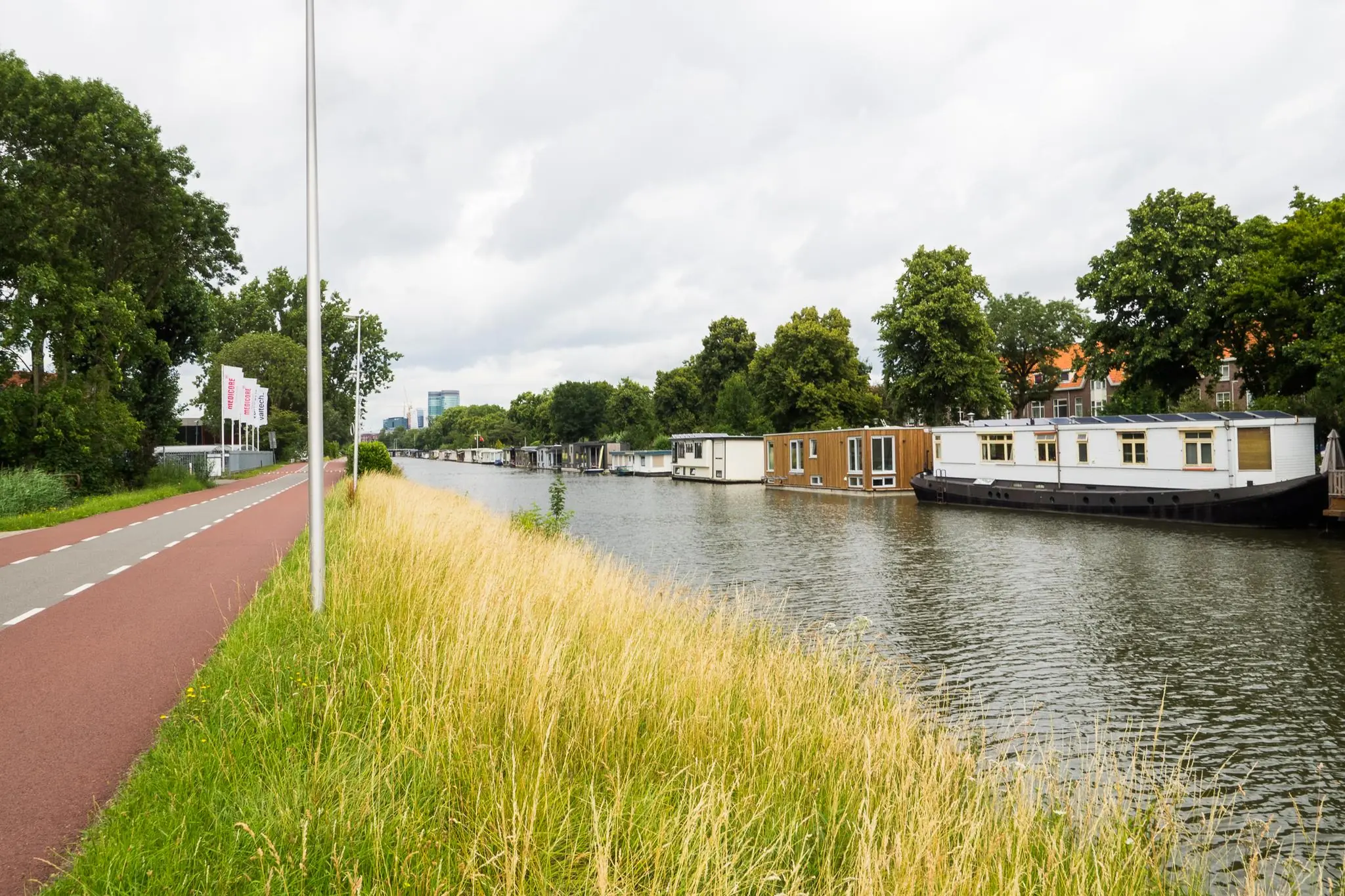 Woonboten langs het kanaal bij de Kanaalweg met een fietspad en grasstrook op de voorgrond.