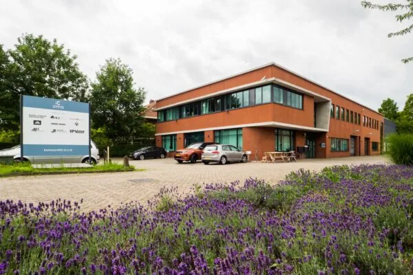 Modern kantoorpand aan de Kanaalweg 22 met parkeerplaatsen, een informatiebord en bloeiende paarse lavendel op de voorgrond.