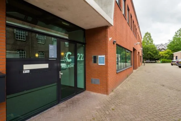 Ingang van een modern kantoorgebouw aan de Kanaalweg 22B met rode bakstenen gevel en glazen deur met welkomsttekst.