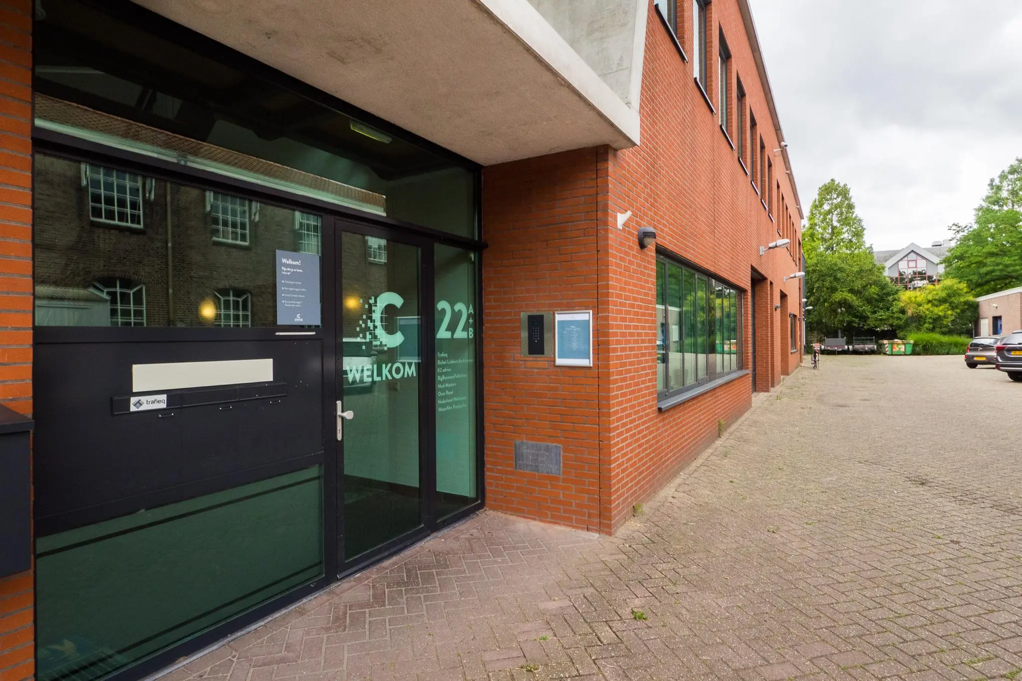 Ingang van een modern kantoorgebouw aan de Kanaalweg 22B met rode bakstenen gevel en glazen deur met welkomsttekst.