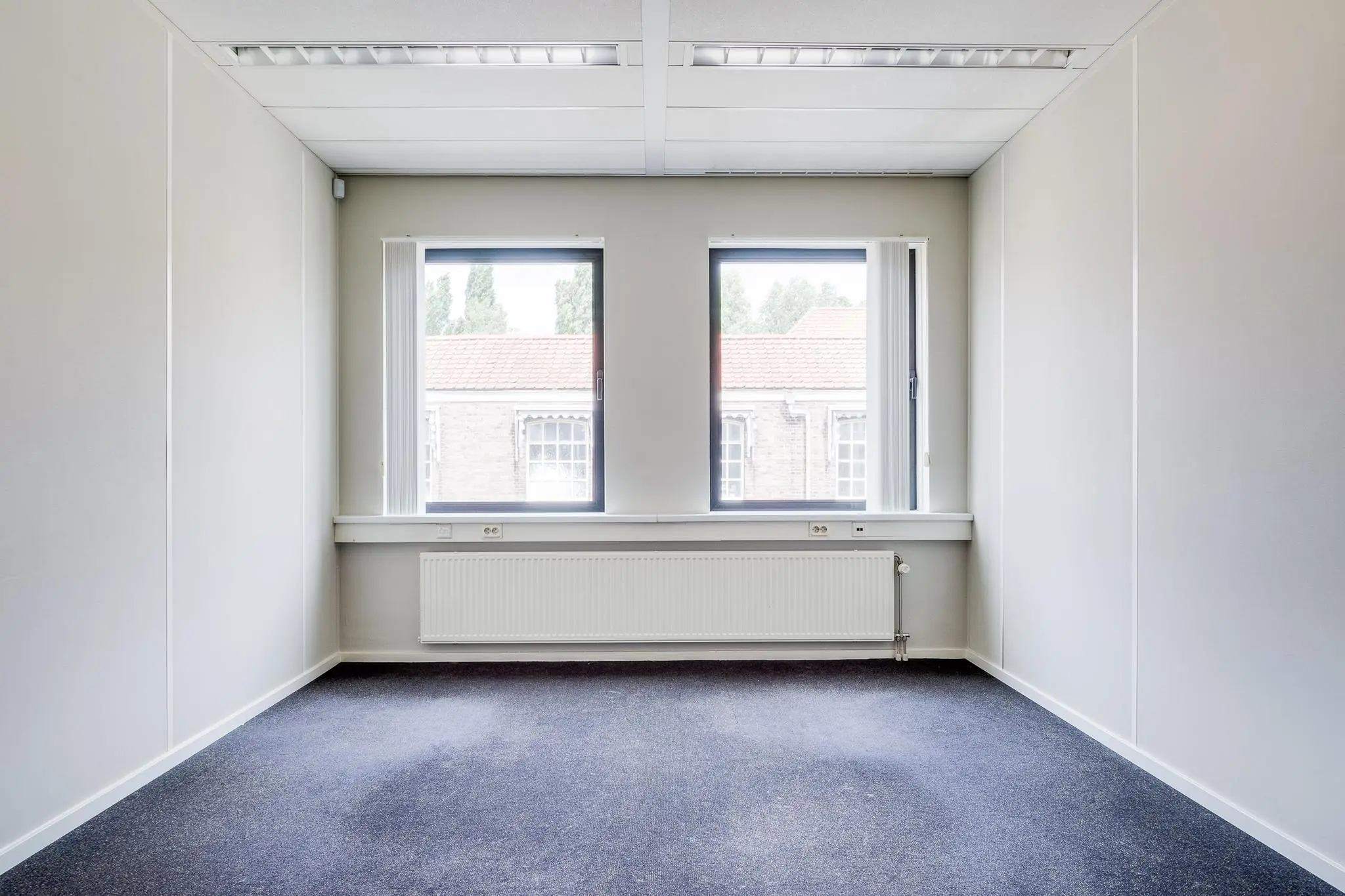 Lege kantoorruimte aan de Kanaalweg met twee ramen en grijsblauwe vloerbedekking.