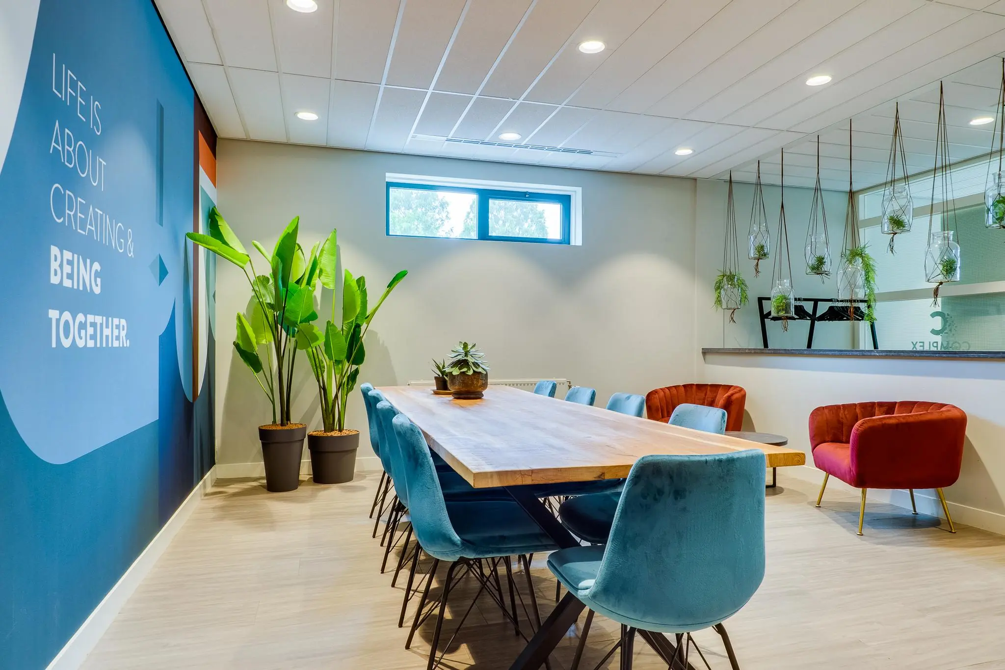 Moderne vergaderruimte aan de Kanaalweg met lange houten tafel, blauwe stoelen, hangplanten en opvallende wandtekst.