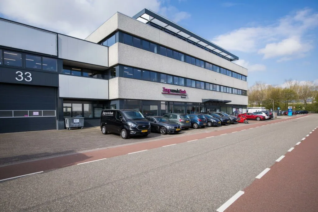 Kantoorpand van Zorg van de Zaak aan de Zonnebaan met geparkeerde auto's op de voorgrond.