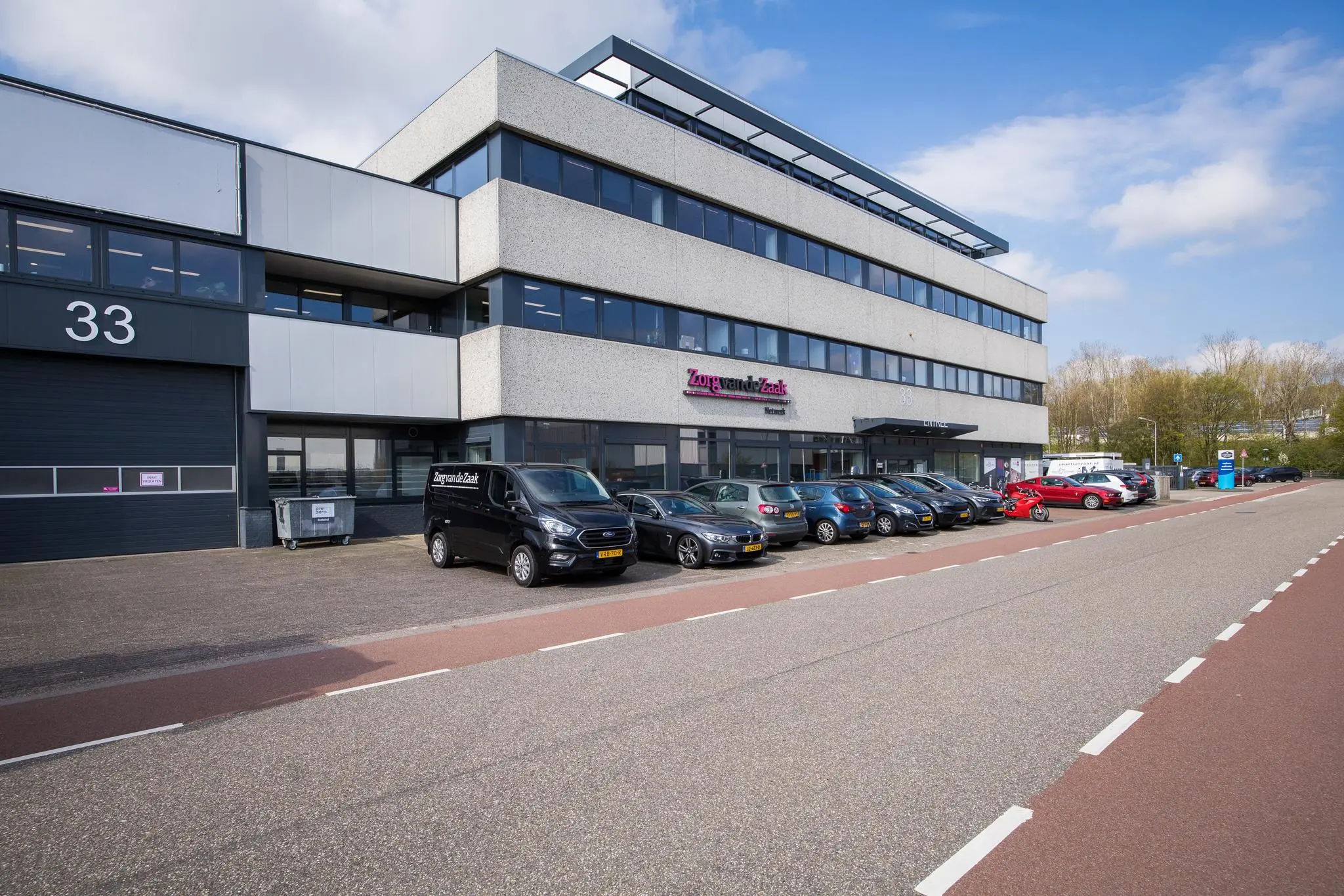 Kantoorpand van Zorg van de Zaak aan de Zonnebaan met geparkeerde auto's op de voorgrond.