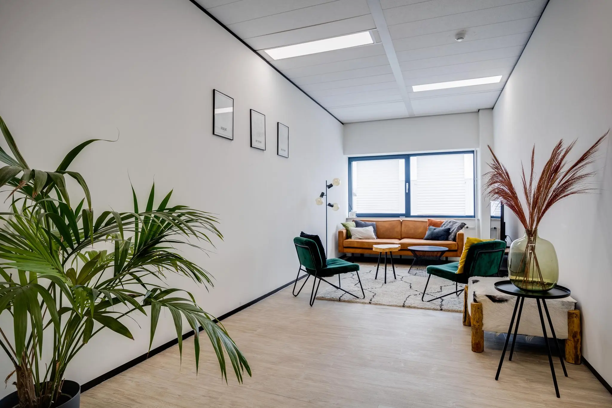 Stijlvol ingerichte wachtruimte aan de Zonnebaan met een cognackleurige bank, groene stoelen en moderne decoratie.