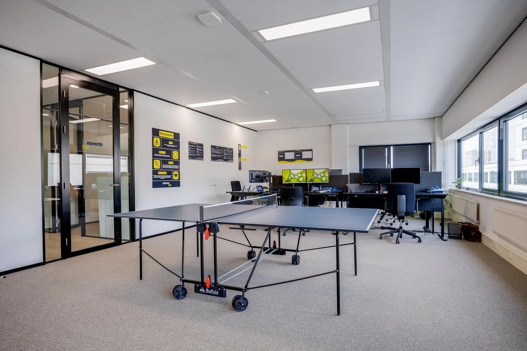 Modern kantoor met werkplekken, een tafeltennistafel en branding van Zonnebaan aan de muur.