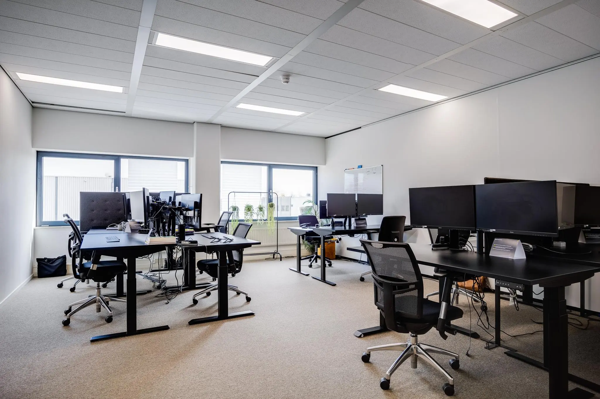 Modern kantoor met meerdere bureaus, bureaustoelen, computerschermen en grote ramen aan de Zonnebaan.