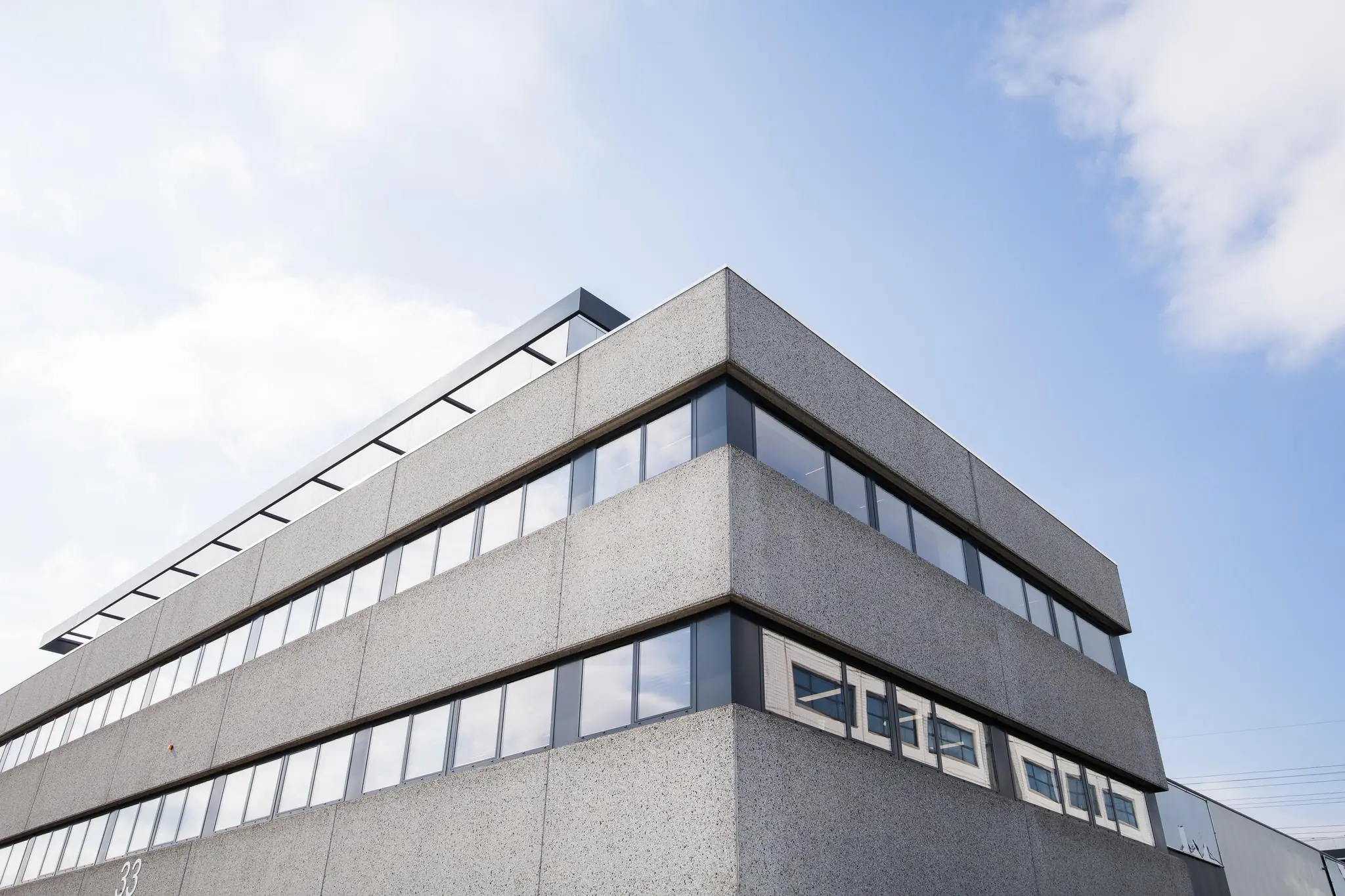 Modern kantoorgebouw aan de Zonnebaan met grijze gevel en grote ramen tegen een blauwe lucht.