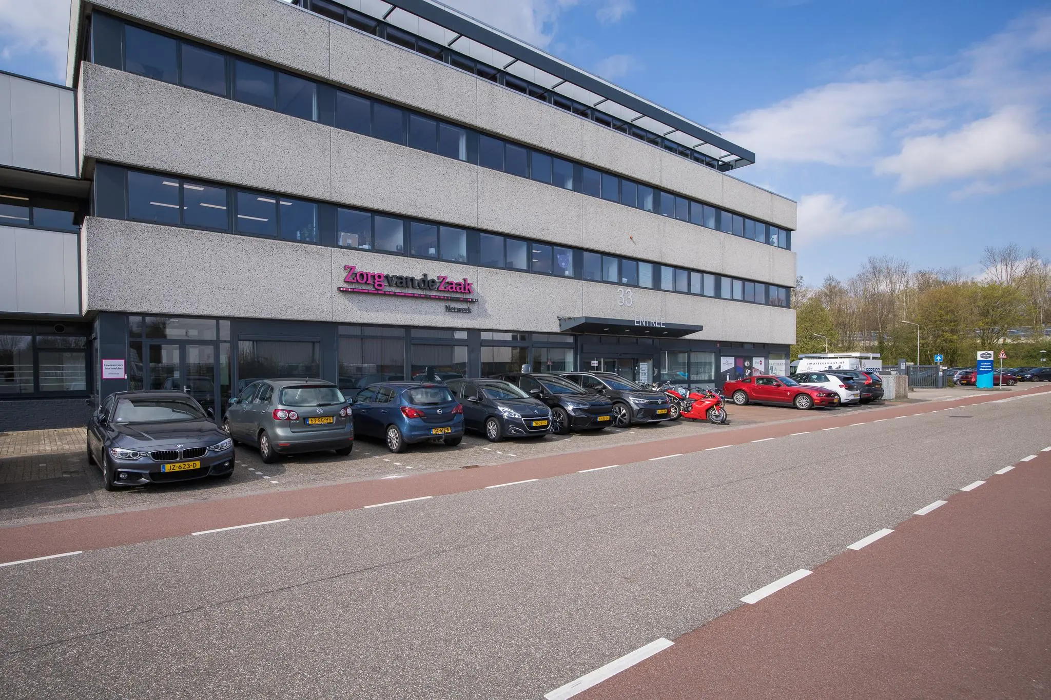 Kantoorpand aan de Zonnebaan 33 met het logo van Zorg van de Zaak en geparkeerde auto's ervoor.
