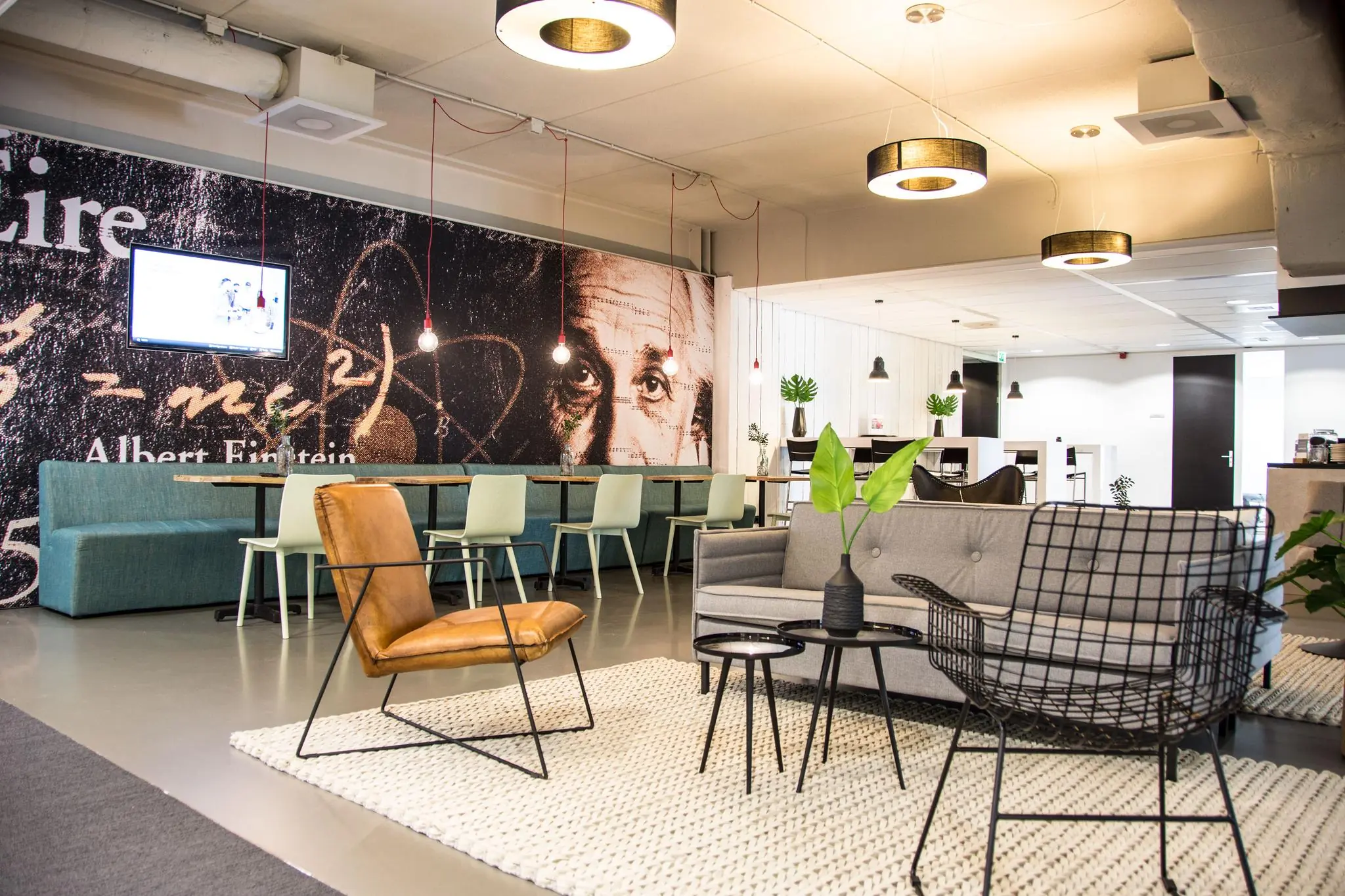 Moderne lounge- en werkruimte met zitgedeelte, wanddecoratie van Albert Einstein en strakke industriële inrichting aan de Meidoornkade.