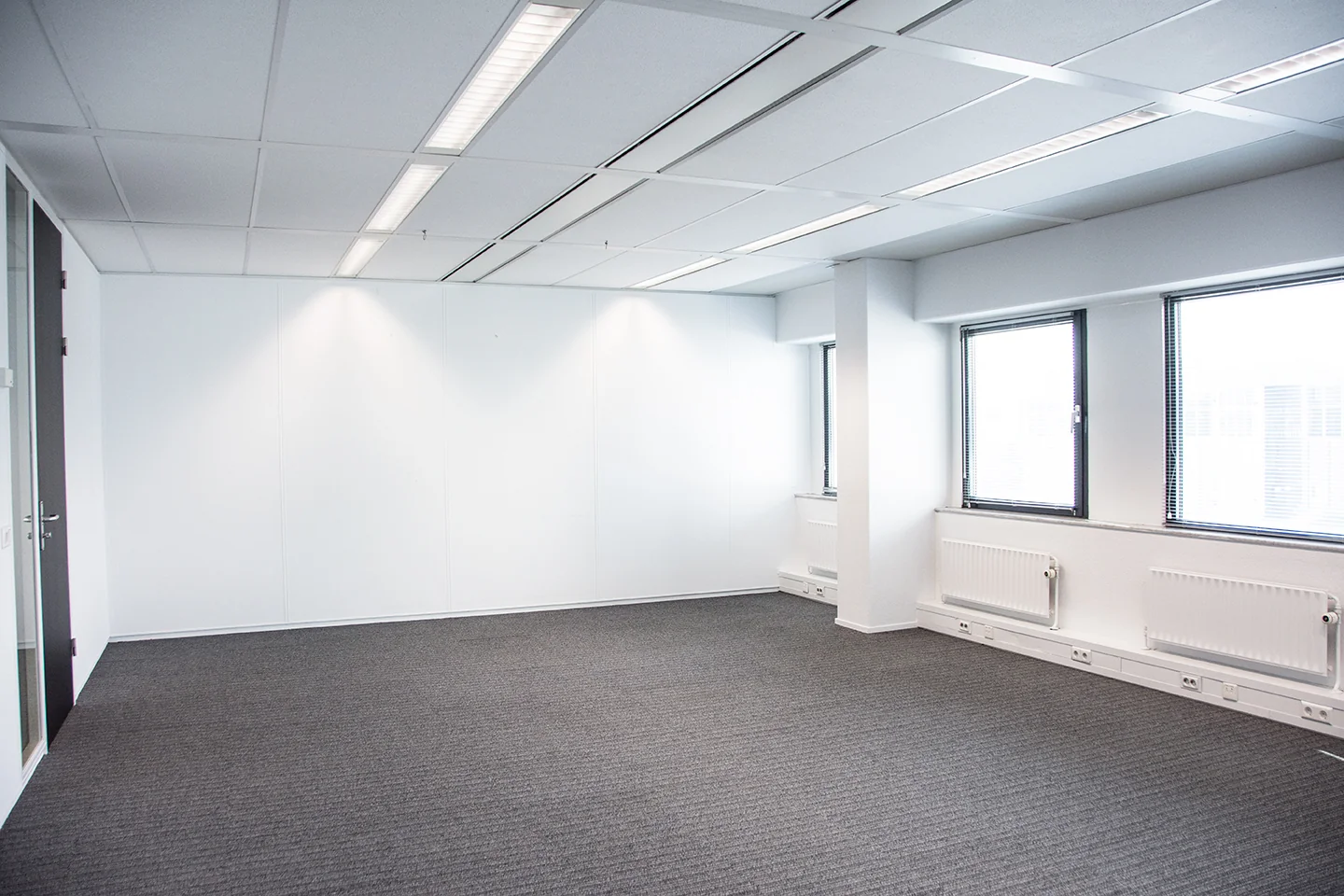 Lichte, lege kantoorruimte aan de Meidoornkade met grijs tapijt en grote ramen.