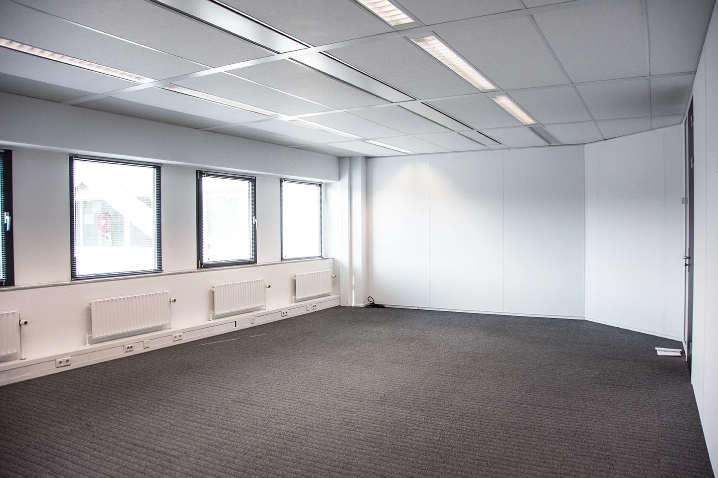 Leeg kantoor met grijze vloerbedekking, witte muren en meerdere ramen aan de Meidoornkade.