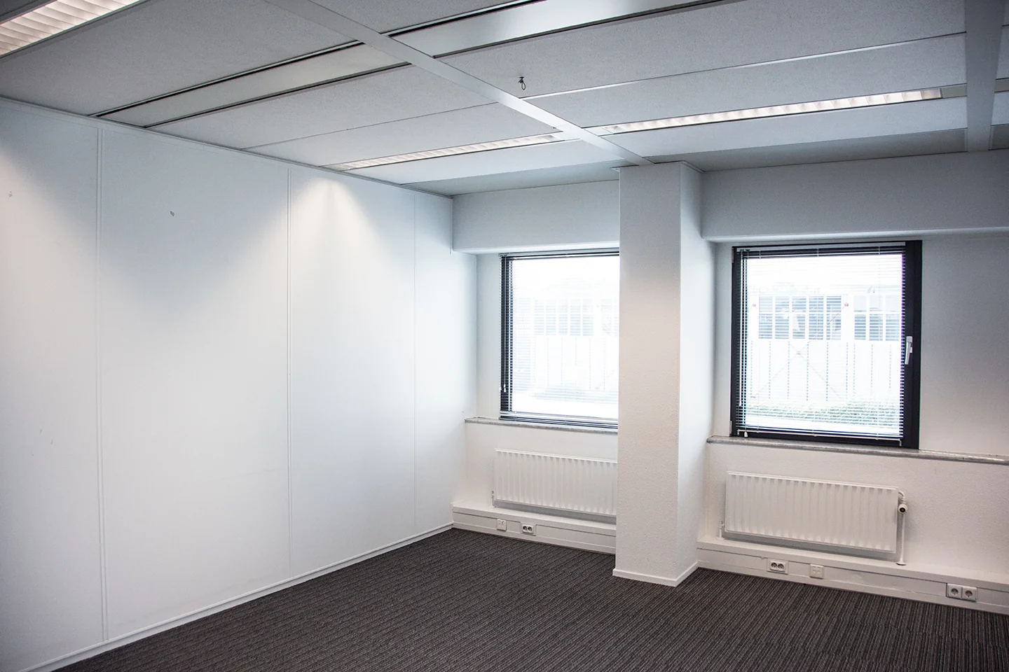Licht en leeg kantoor aan de Meidoornkade met twee ramen en een grijze tapijtvloer.