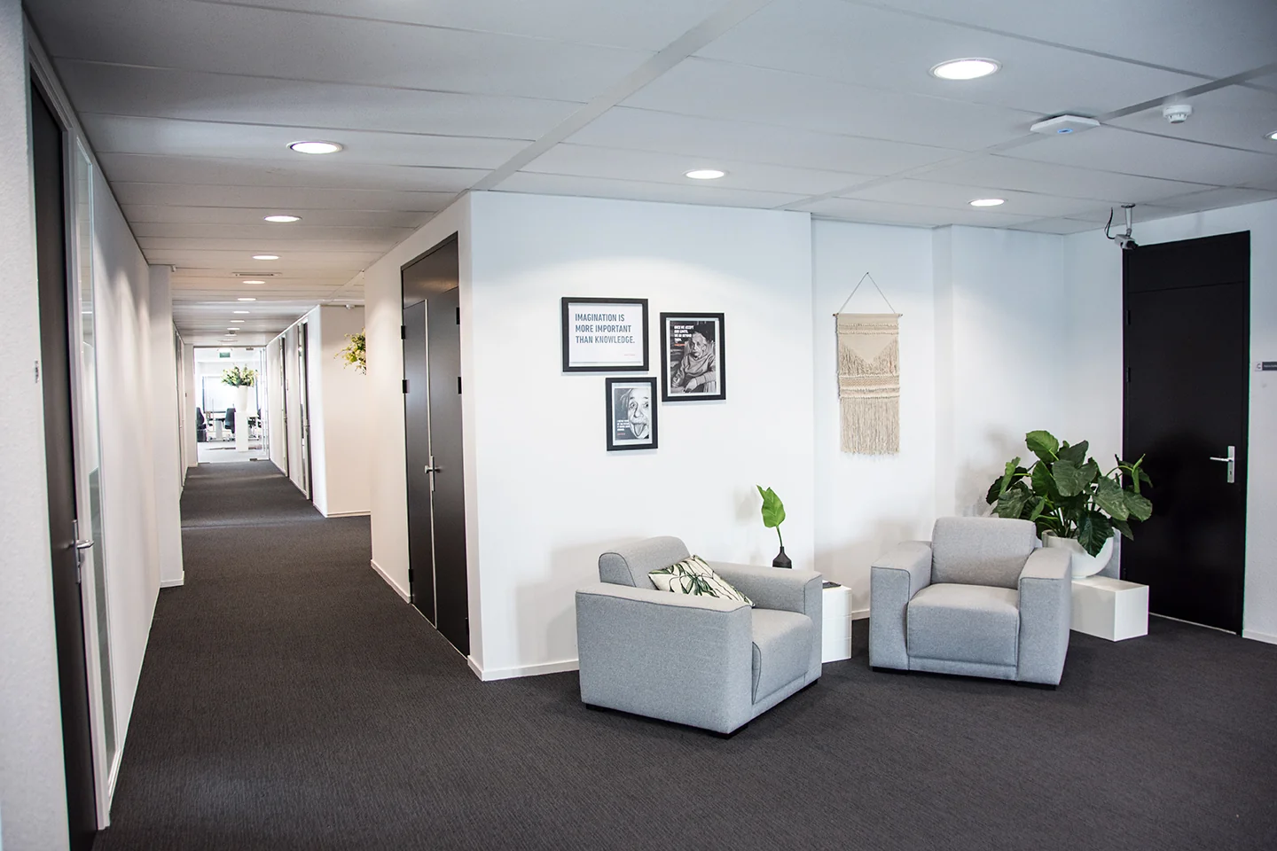 Moderne en lichte kantoorhal aan de Meidoornkade met twee grijze fauteuils, muurdecoratie en groene planten.