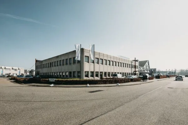 Kantoorpand aan de Meidoornkade met parkeerplaatsen en vlaggenmasten op een zonnige dag.