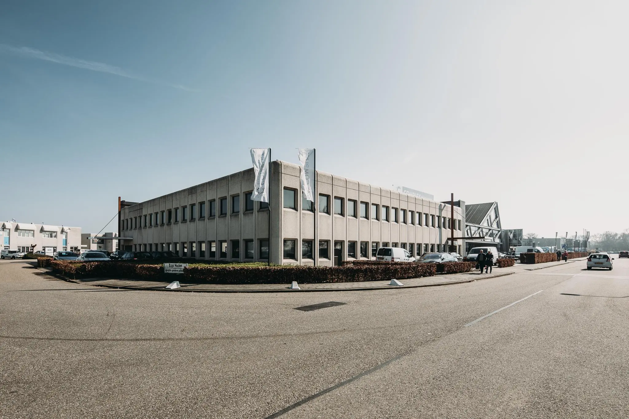 Kantoorpand aan de Meidoornkade met parkeerplaatsen en vlaggenmasten op een zonnige dag.