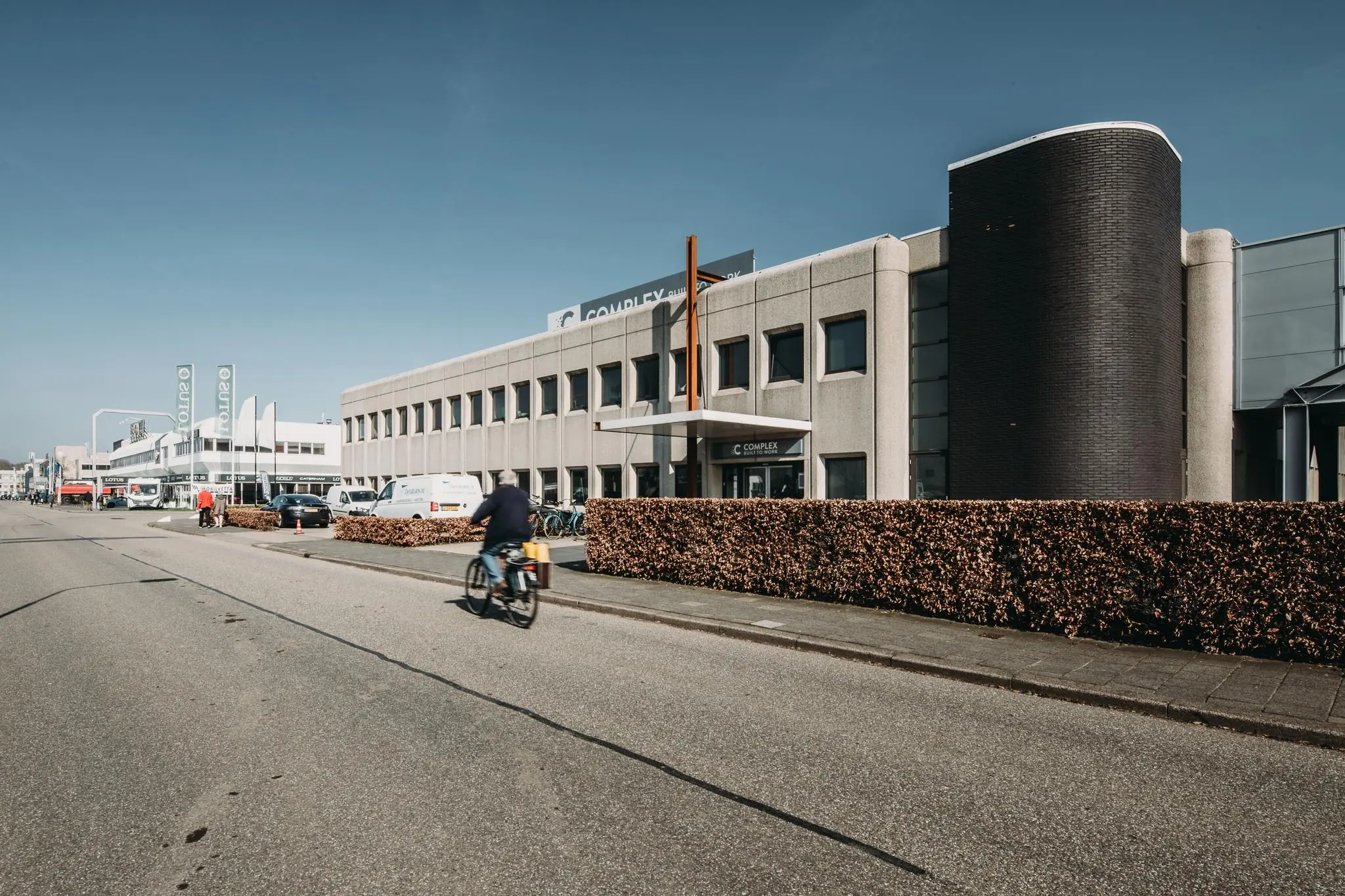 Bedrijfsgebouw aan de Meidoornkade met fietsen, geparkeerde auto’s en een fietser op de voorgrond.