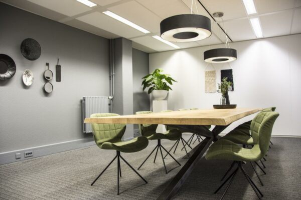 Moderne vergaderruimte aan de Meidoornkade met houten tafel, groene stoelen en strakke, stijlvolle inrichting.