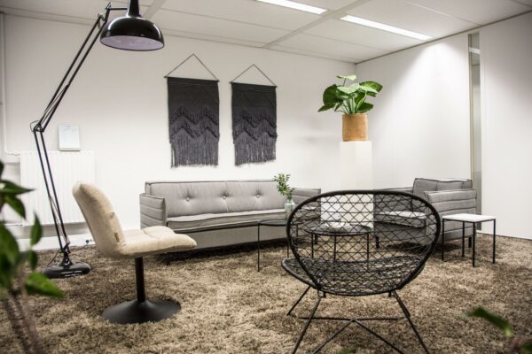 Moderne wachtruimte aan de Meidoornkade met grijze zitmeubels, een groot vloerkleed en opvallende wanddecoratie.