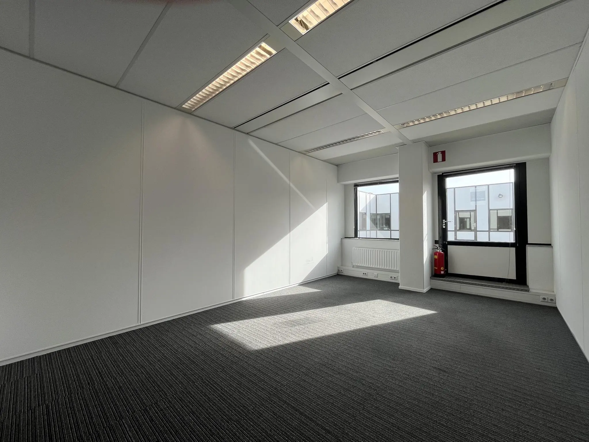 Licht en leeg kantoorruimte aan de Meidoornkade met grijs tapijt en grote ramen.