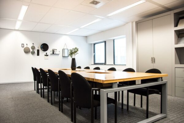 Vergaderruimte met een houten tafel, zwarte stoelen en moderne wanddecoratie aan de Meidoornkade.