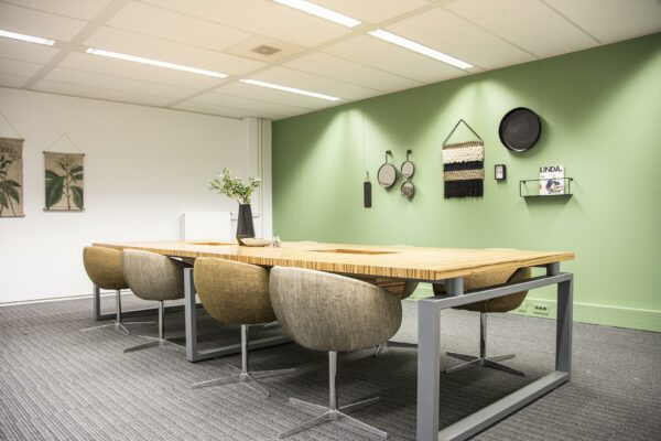 Moderne vergaderruimte aan de Meidoornkade met houten tafel, gestoffeerde stoelen en groene accentmuur met decoratieve wandobjecten.