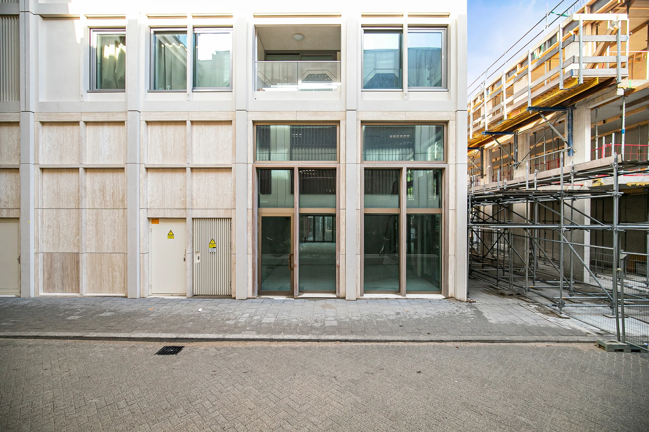 Modern commercial building facade with large glass doors and windows, located next to a construction site on Baan street.