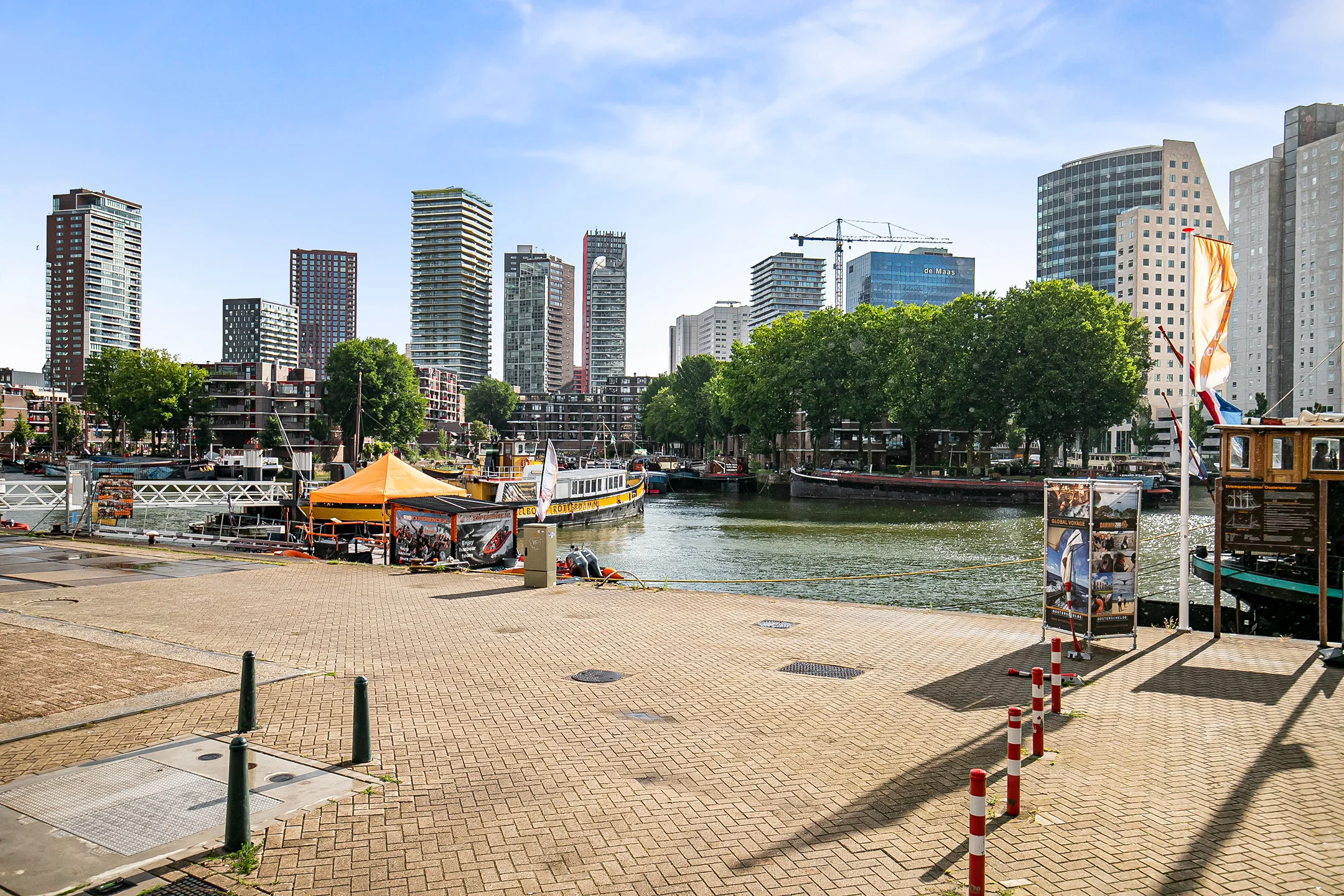 View of a modern harbor area in Rotterdam with high-rise buildings, boats, and a quay with promotional stands.