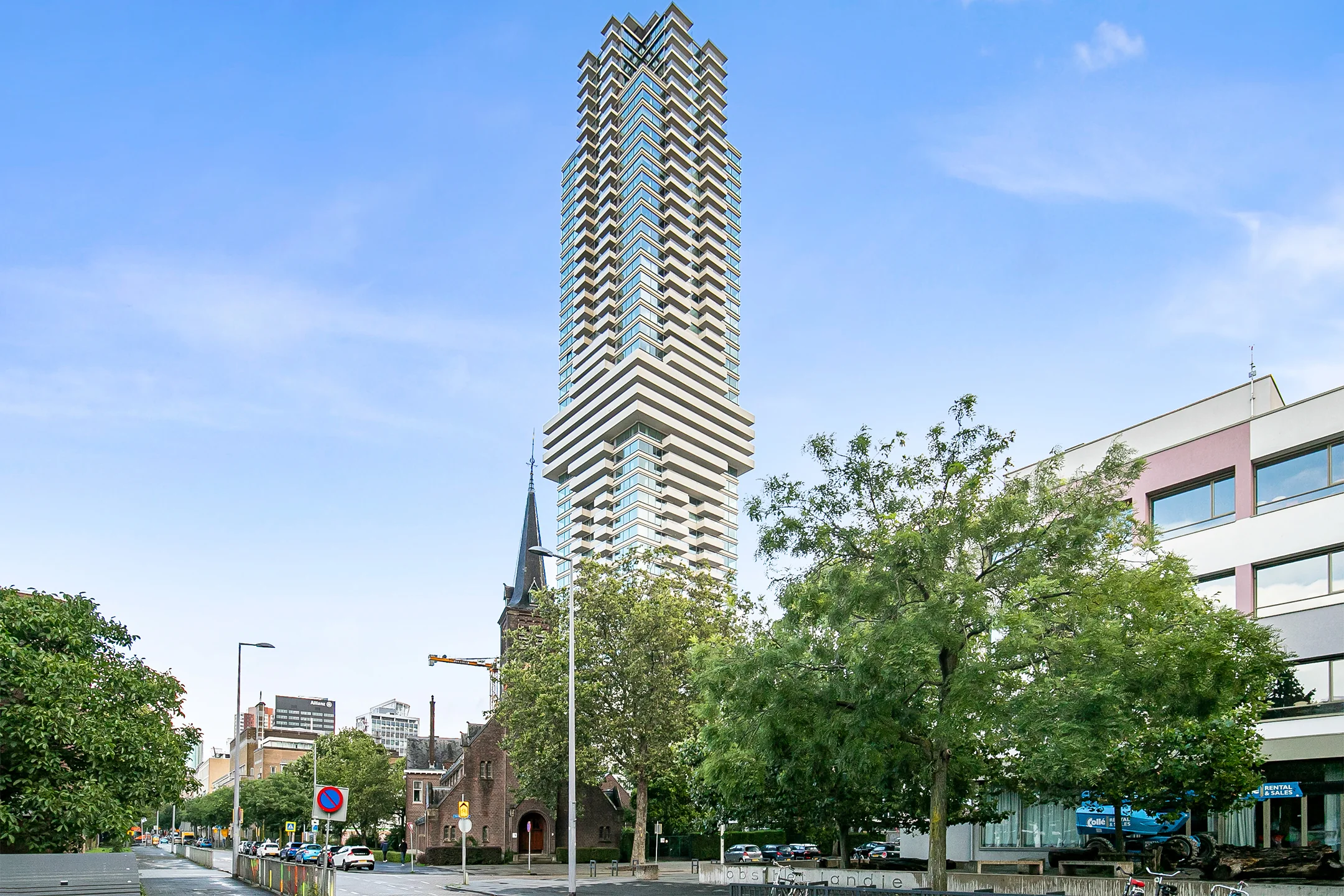 Modern high-rise residential tower 'De Zalmhaven' in Rotterdam, with a historic church and city street in the foreground.