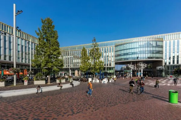 Modern plein bij Hoekenrode in Amsterdam met mensen, bomen en omliggende kantoorpanden.