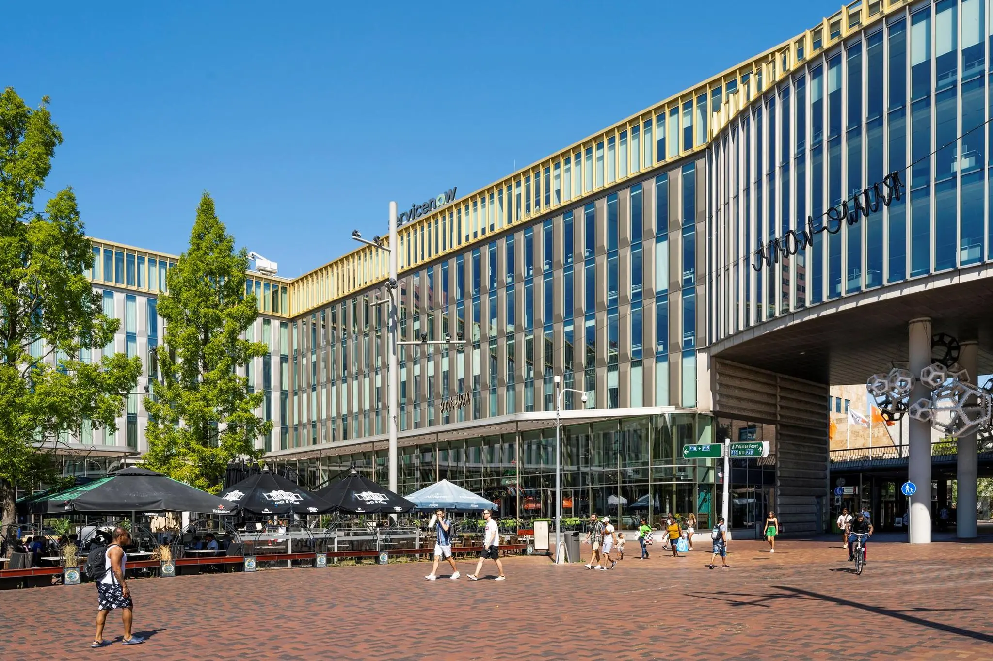 Modern kantoorgebouw Hoekenrode met winkels en terrassen op een zonnig plein in Amsterdam-Zuidoost.