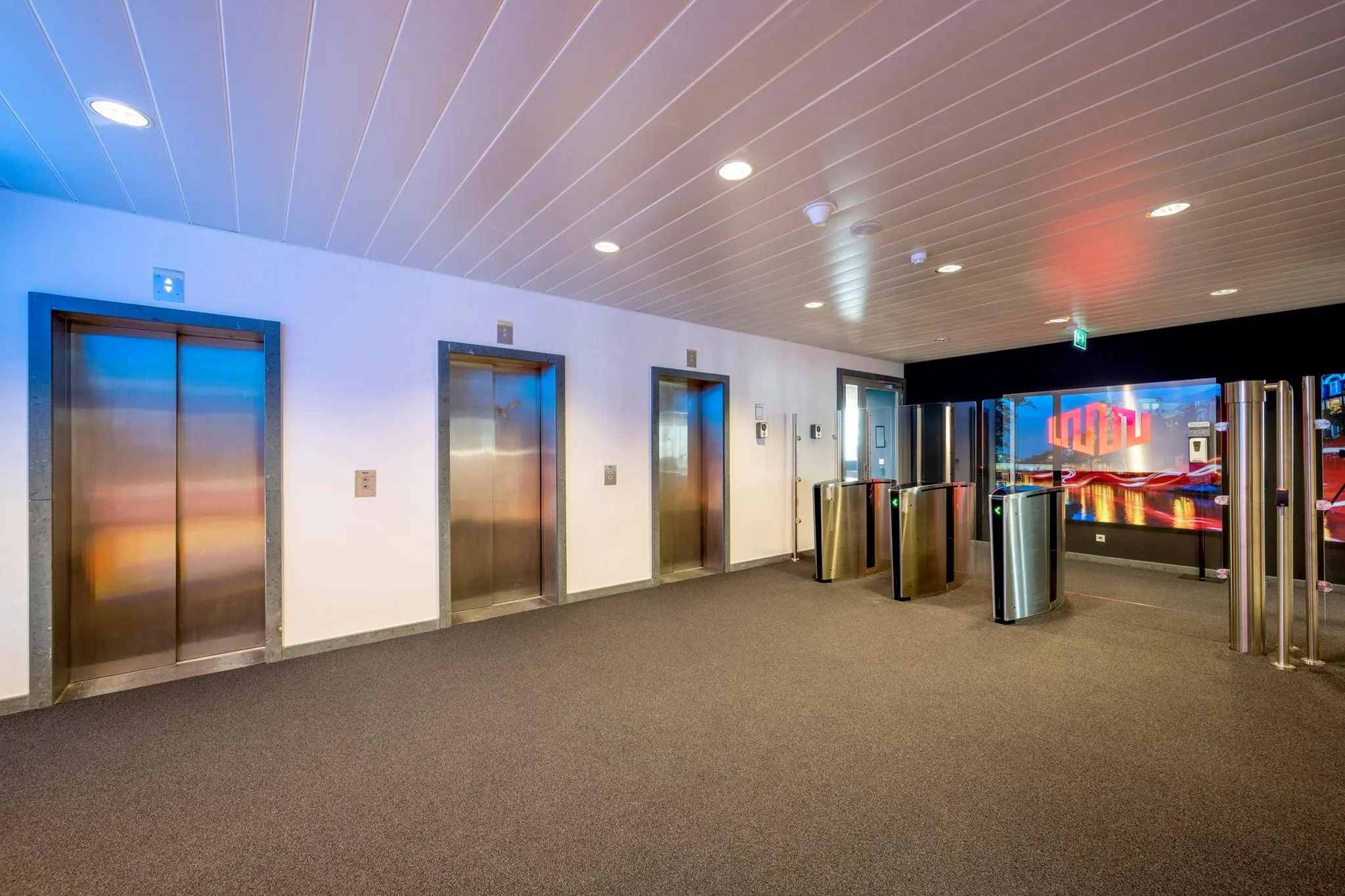 Moderne entreehal van gebouw Hoekenrode met drie liften en beveiligde toegangspoortjes.