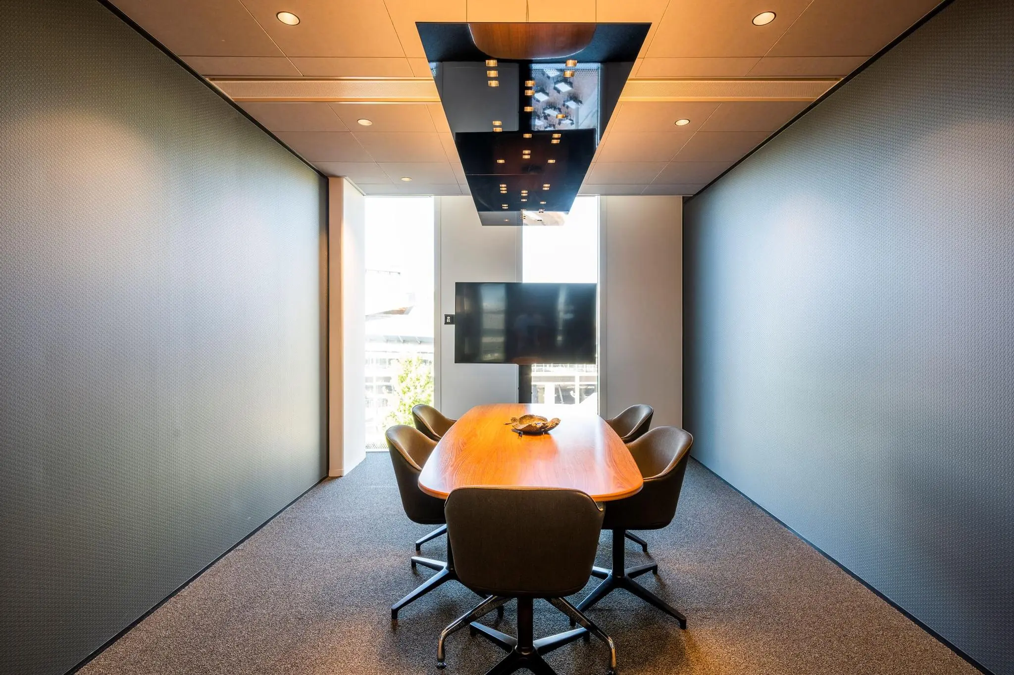 Moderne vergaderruimte in Hoekenrode met ovale houten tafel, vijf stoelen en een flatscreen-tv aan de muur.