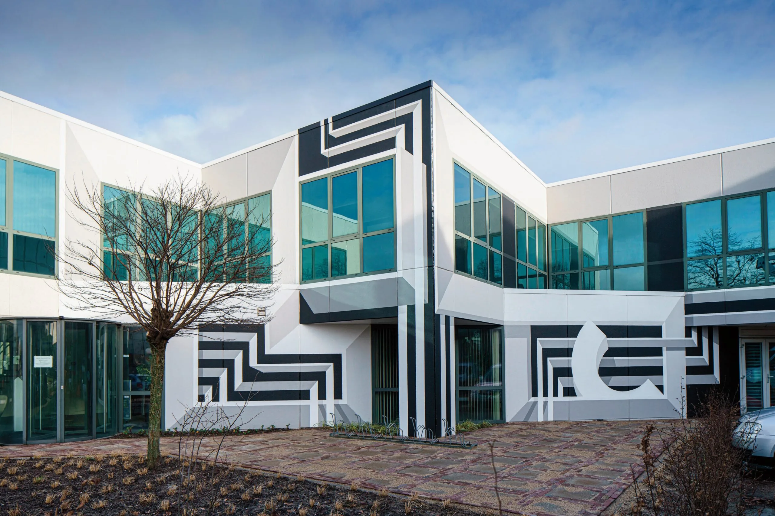 Modern white office building on Rietbaan with geometric black artwork and large blue-tinted windows.