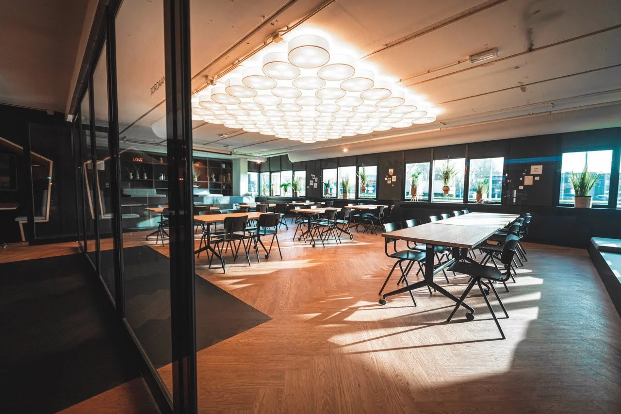 Modern cafeteria with wooden floors, large windows, and circular ceiling lights at Rietbaan 176.