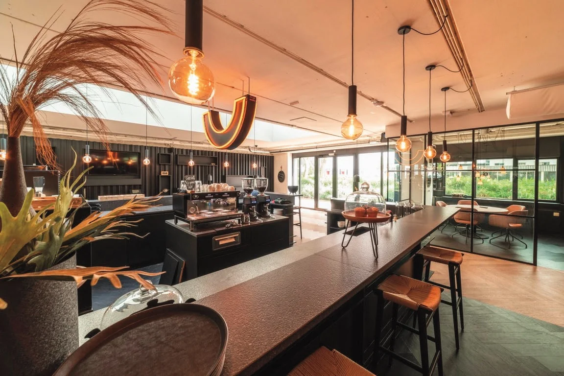 Modern café interior at Rietbaan with stylish lighting, coffee machines, and a sleek bar area.