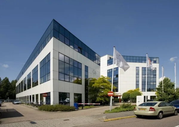 Modern wit kantoorgebouw met spiegelende ramen aan de Rietbaan in een groene en zonnige omgeving.