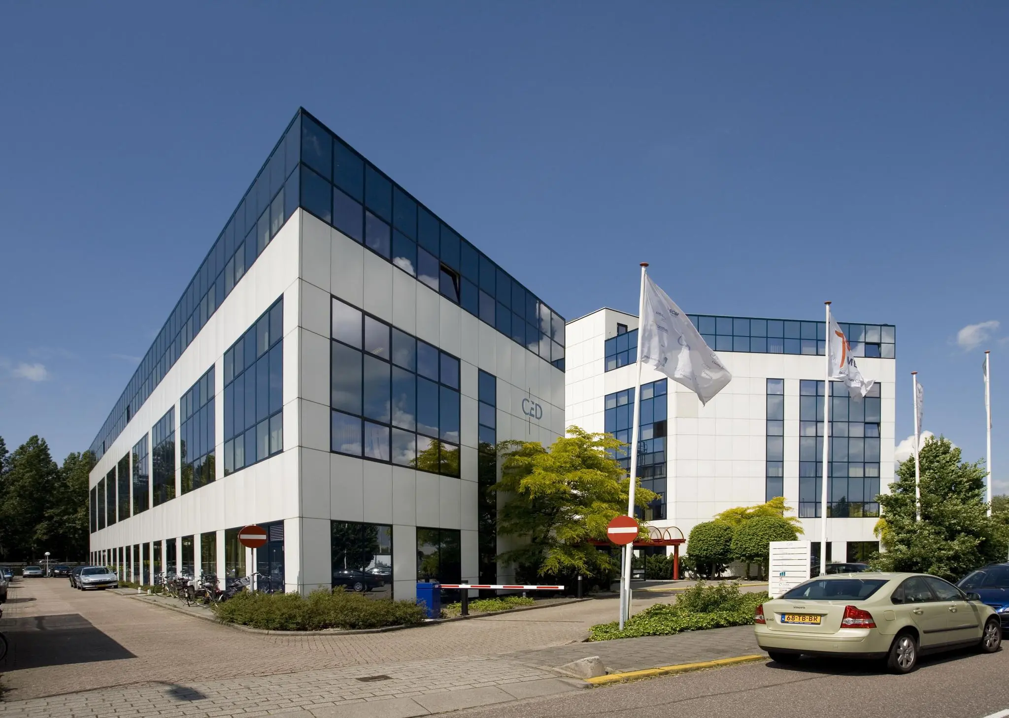 Modern wit kantoorgebouw met spiegelende ramen aan de Rietbaan in een groene en zonnige omgeving.