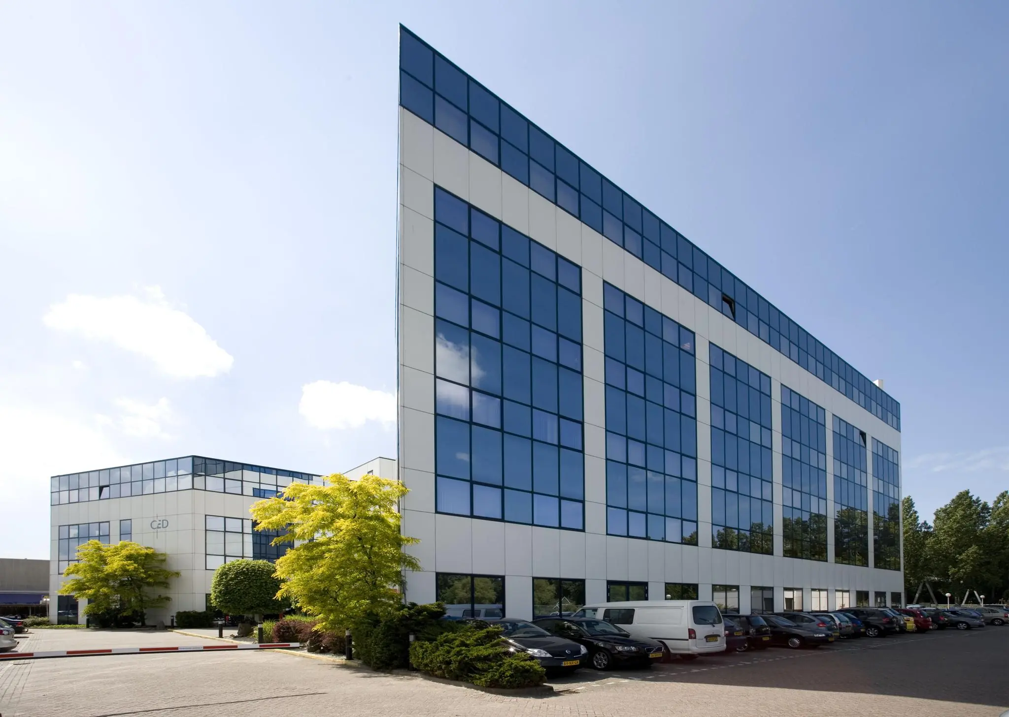 Modern kantoorgebouw aan de Rietbaan met spiegelende ramen en parkeerplaats op de voorgrond.