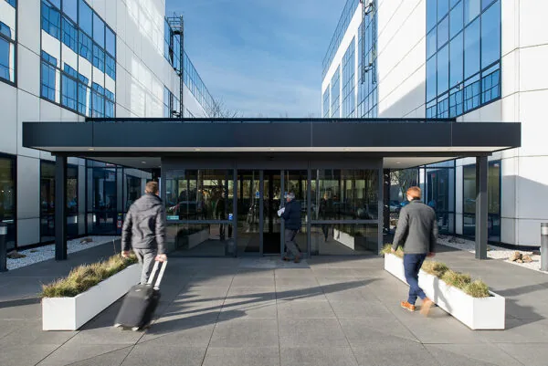 Ingang van een modern kantoorgebouw aan de Rietbaan met mensen die naar binnen lopen.