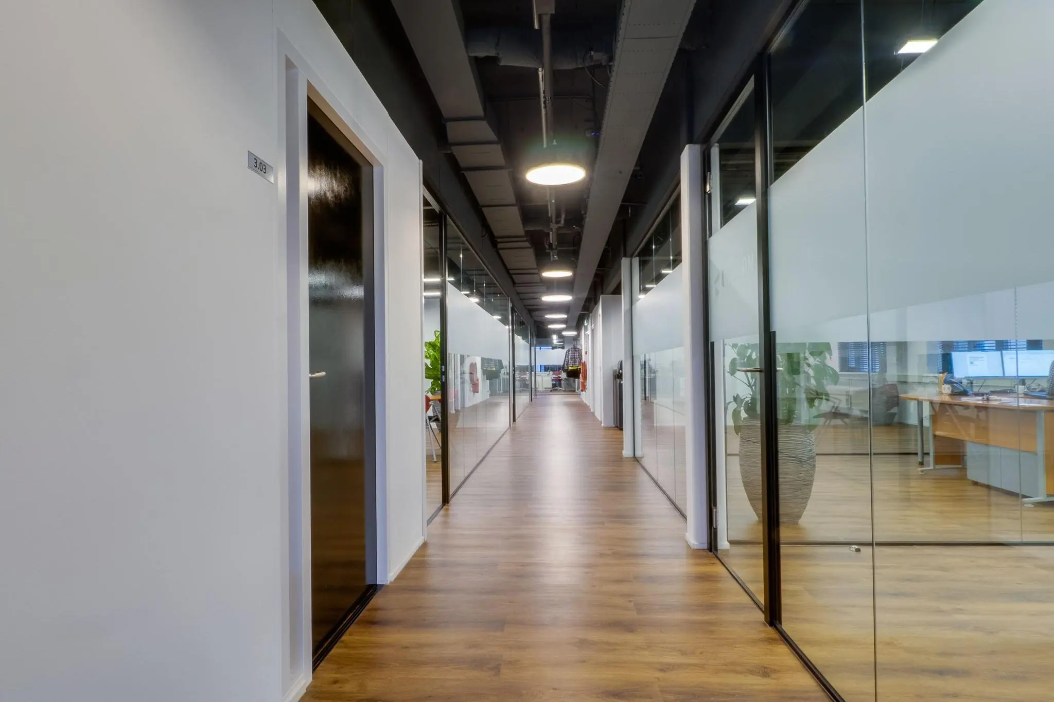 Lange, moderne kantoorruimte aan de Rietbaan met houten vloer, glazen wanden en systeemplafond.