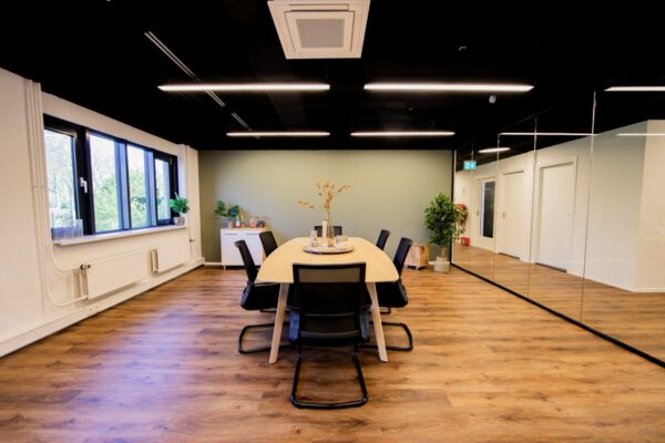 Moderne vergaderruimte aan de Rietbaan met houten vloer, lange tafel, zwarte stoelen en groene accenten.