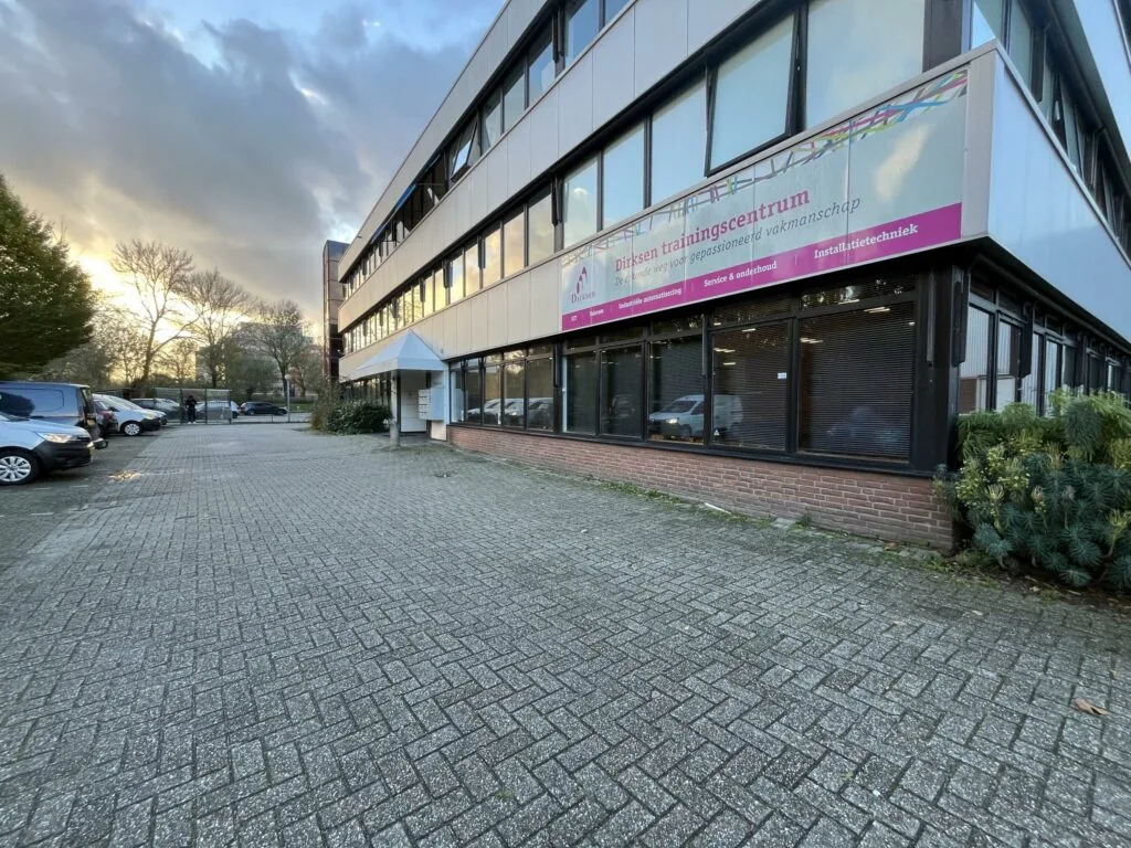 Vooraanzicht van het Dirksen Trainingscentrum aan de Industrieweg met parkeerplaats en enkele geparkeerde auto's.