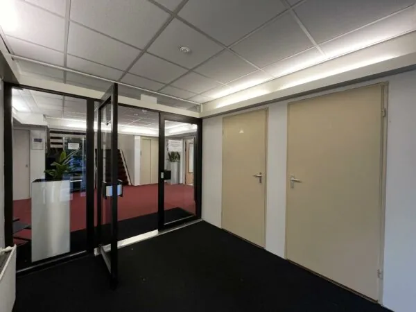Hal met glazen deuren, beige binnendeuren en rood tapijt in een kantoorpand aan de Industrieweg.