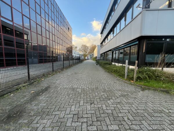 Een smalle, met klinkers bestrate weg tussen twee moderne bedrijfsgebouwen aan de Industrieweg.
