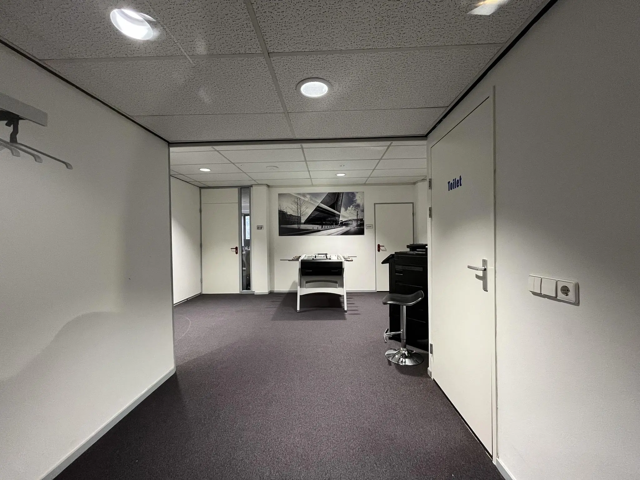 Binnenruimte van een kantoorpand aan de Industrieweg met zicht op een hal, toiletdeur en werktafel.