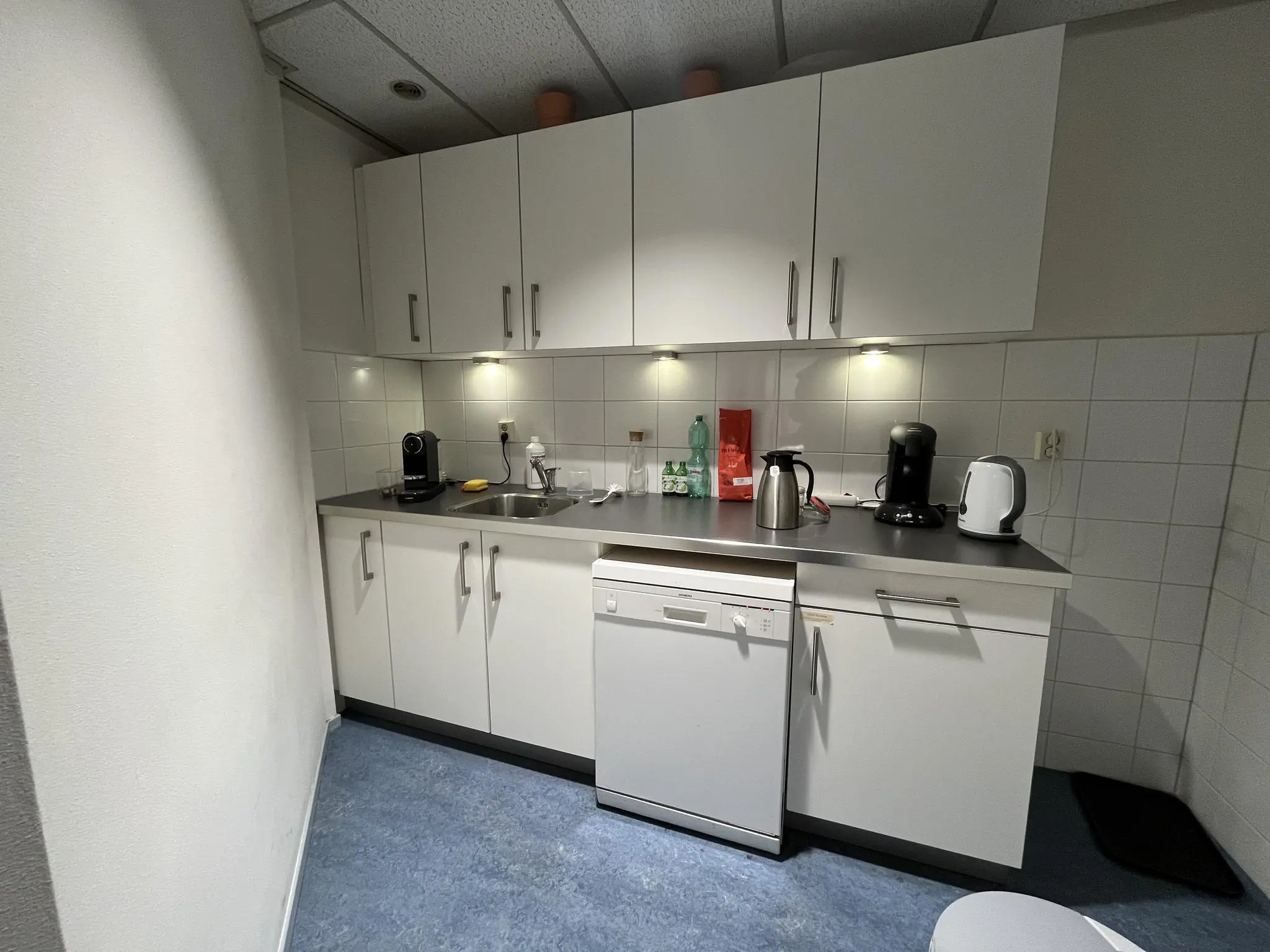 Kleine pantry-keuken op een kantoor aan de Industrieweg met witte kastjes, koffiemachines en een vaatwasser.
